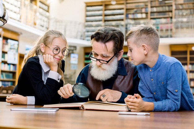 Anciano profesor profesor concentrado y sus dos pequeños estudiantes lindos inteligentes que leen el libro juntos.