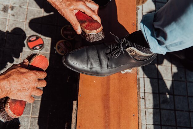 Foto un anciano pulindo a mano y pintando un zapato negro en la calle.