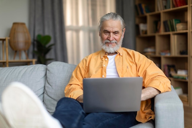 Un anciano relajado usando una laptop mientras se relaja en casa