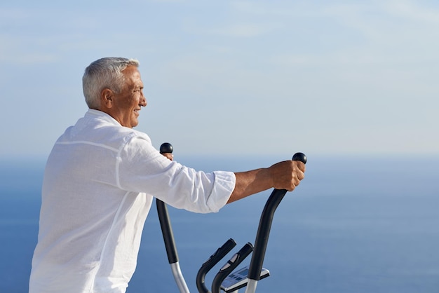 un anciano sano haciendo ejercicio en una máquina caminadora de gimnasio en una moderna terraza casera con vista al mar