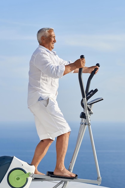 un anciano sano haciendo ejercicio en una máquina caminadora de gimnasio en una moderna terraza casera con vista al mar