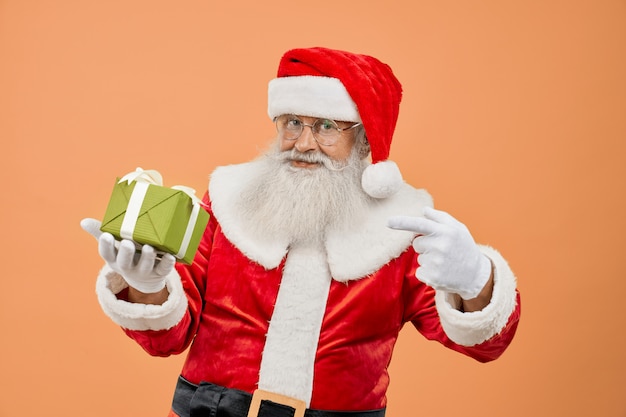 Anciano Santa Claus mirando a cámara y apuntando en caja de regalo