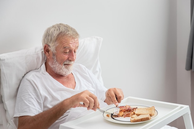 Anciano senior hombre desayunando en la cama en el dormitorio en el hogar de ancianos