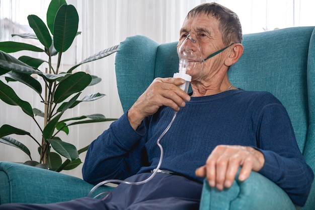 Anciano senior se sienta en un sillón con una máscara de oxígeno en cuarentena