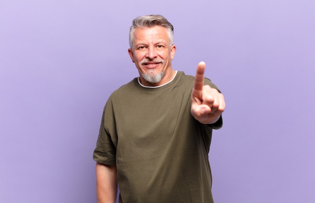 Anciano senior sonriendo con orgullo y confianza haciendo la pose número uno triunfalmente, sintiéndose como un líder