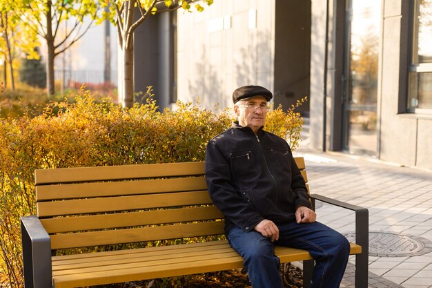 Anciano sentado en un banco en el parque de otoño.