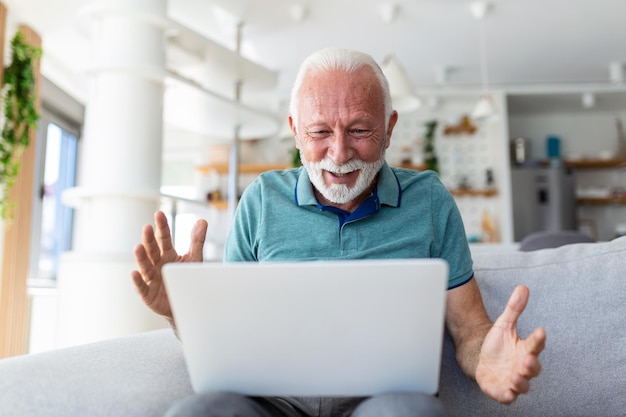 Anciano sentado en el sofá mirando la pantalla de la computadora portátil gritar con alegría se siente emocionado feliz celebrando la victoria de la lotería momento afortunado obtuvo oportunidad en línea ventas y descuentos concepto de comercio electrónico