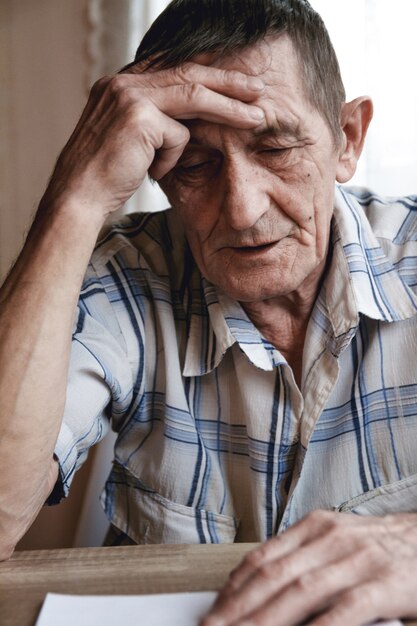 Anciano sentado sosteniendo su cabeza, sufriendo pérdida de memoria