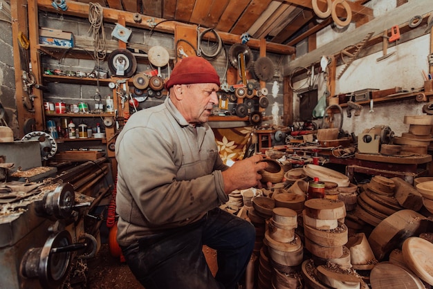 Un anciano sentado en el taller y untando utensilios de madera con aceite de linaza.