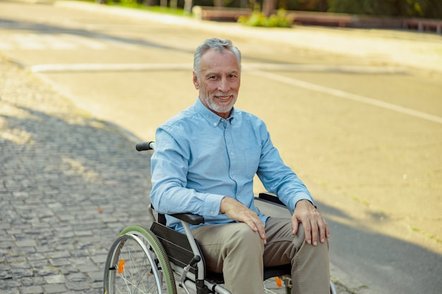 Anciano en silla de ruedas sonriendo a la cámara mientras viaja solo en el parque en un día de verano