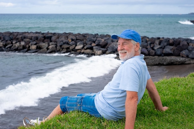 Un anciano sonriente sentado en el césped de la playa en un día de invierno disfrutando de las vacaciones o de la jubilación