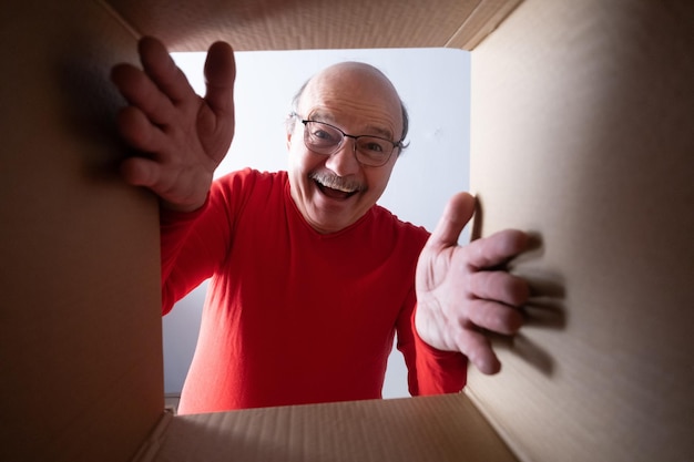 Un anciano sorprendido desempacando, abriendo una caja de cartón y mirando dentro.