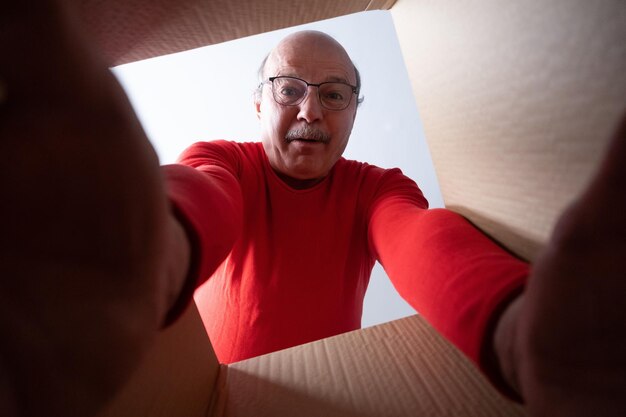 Un anciano sorprendido desempacando, abriendo una caja de cartón y mirando dentro.