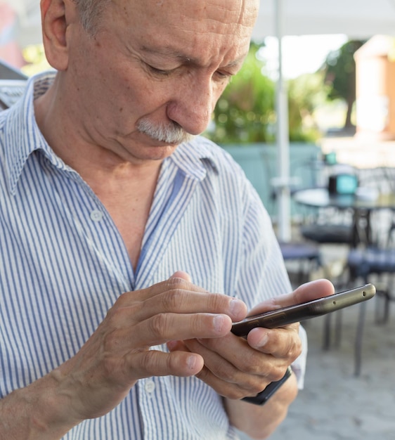 Foto el anciano sostiene un teléfono móvil en sus manos