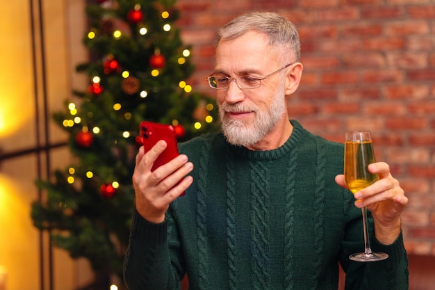 Un anciano con un tejido verde hablando con su familia por conexión de video por teléfono cerca del árbol de Navidad