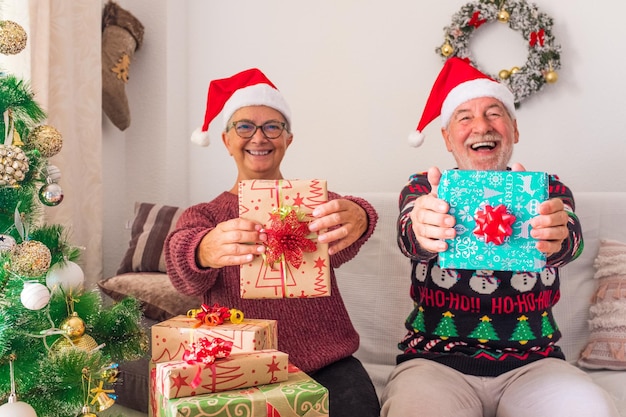 Ancianos divirtiéndose y mostrando a la cámara su regalo o presente ante la cámara - celebrando la Navidad juntos