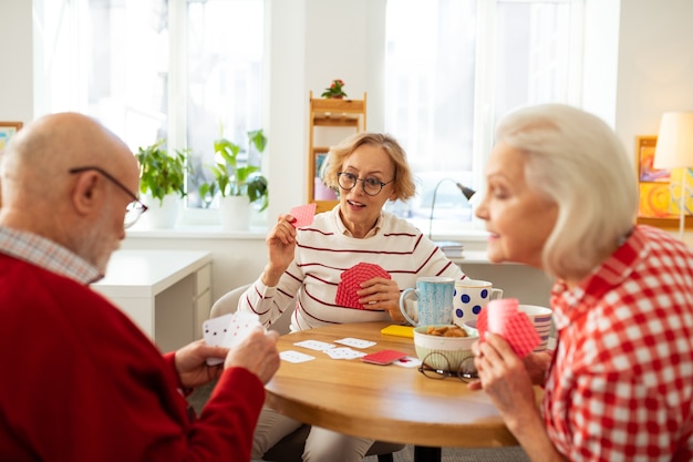 Ancianos guapos sentados alrededor de la mesa redonda mientras juegan juegos de cartas