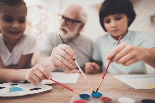 Ancianos y niños sostienen pinceles pintando juntos.