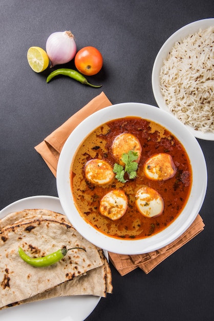 Anda Curry oder Egg Masala Soße, indisches scharfes Essen oder Rezept, serviert mit Jeera Reis, Roti oder Naan, selektiver Fokus. Über bunter oder hölzerner Tischplatte