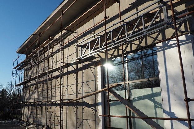 Andaime em uma nova casa de um andar Trabalhos de fachada Edifício comercial Edifício baixo de construção privada Reboco da parede de um edifício Construção de lojas Estruturas de produção de metal