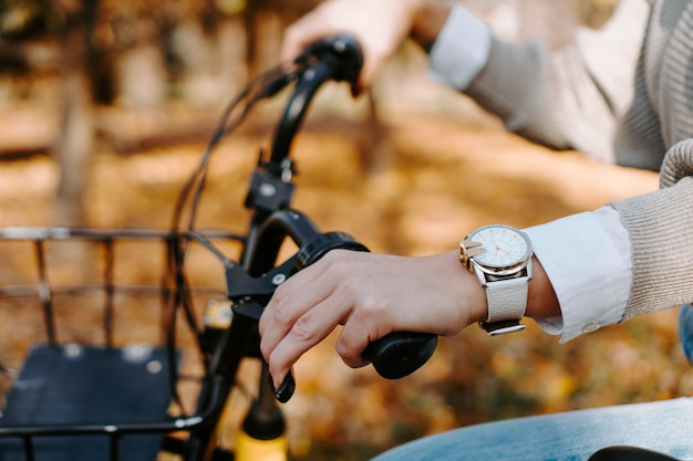 Andar de bicicleta em um dia ensolarado no outono park. Mão feminina em uma roda de bicicleta