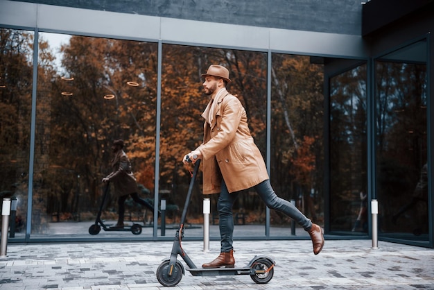 Andar de scooter elétrico Jovem modelo masculino em roupas da moda está ao ar livre na cidade durante o dia