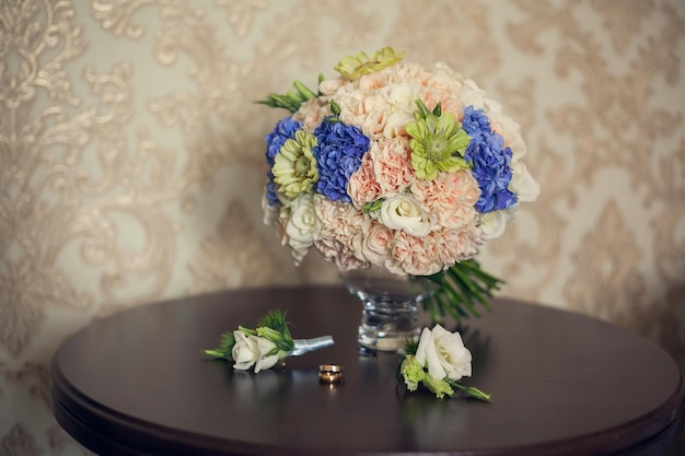 Anéis de casamento de buquê de noiva e lapelas em cima da mesa