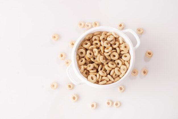 Anéis de cereais saudáveis em um fundo branco em um prato e espalhados sobre a mesa. manhã comer. muesli seco.