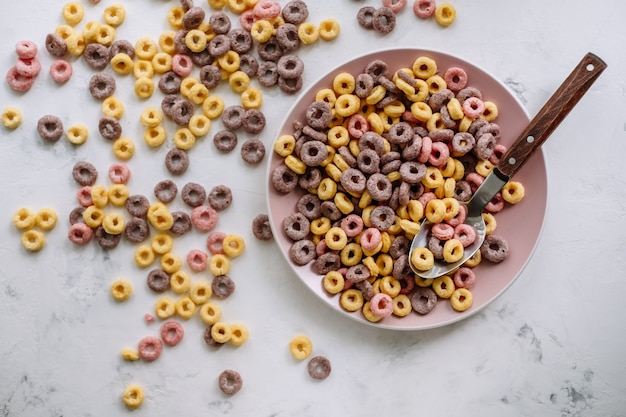 Anéis de milho multicoloridos em um prato rosa no café da manhã, comida saudável.