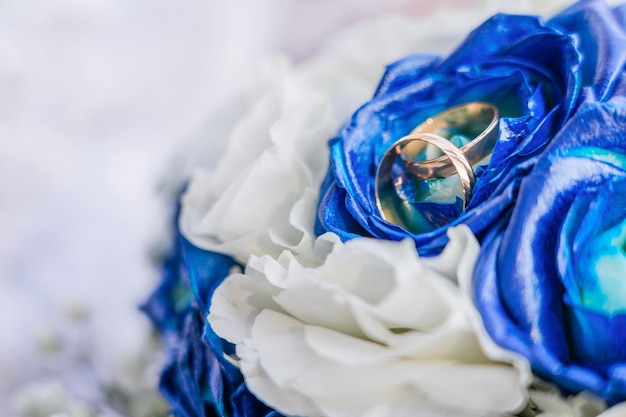 Foto anéis de ouro de casamento em um buquê de rosas brancas e azuis copiar espaço