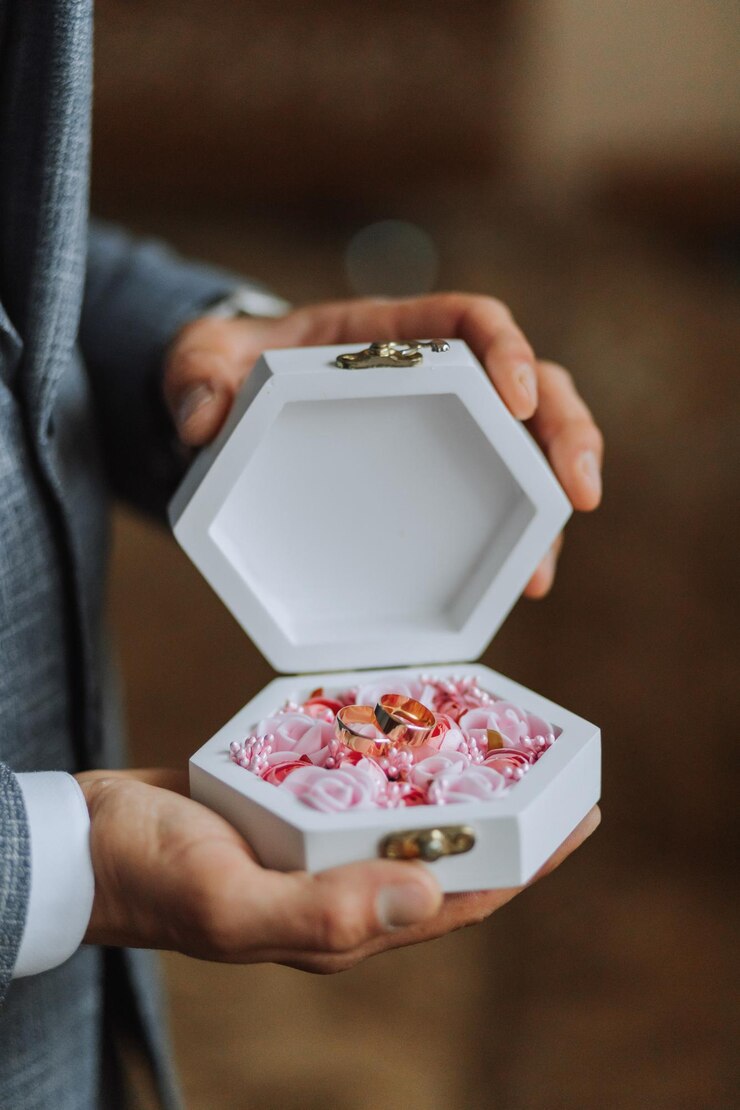 Foto anéis de ouro de casamento em uma caixa branca decorativa com flores cor-de-rosa nas mãos do noivo close-up conceito de jóias
