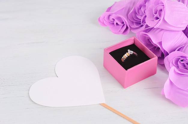 Anel de diamante dourado em caixa rosa com buquê de rosas