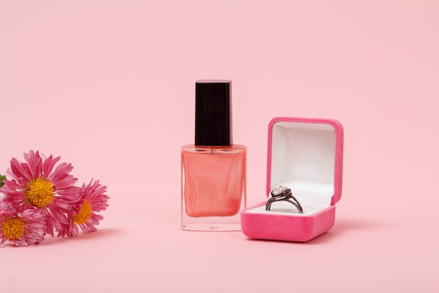 Anel em uma caixa, esmalte, flores em fundo rosa. Joias femininas, cosméticos e acessórios.