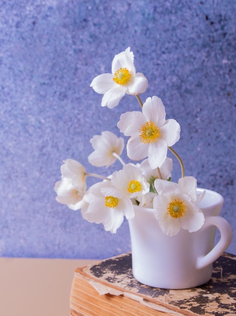 Anemonenblumenstrauß in einer Tasse und Weinbuch Frühlingsmuttertag oder Stilllebenkomposition am 8. März