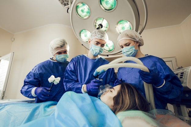 Anestesia del paciente antes de la operación. Tres cirujanos trabajando. Los médicos se están preparando para la cirugía. Cirujanos y paciente en el hospital.