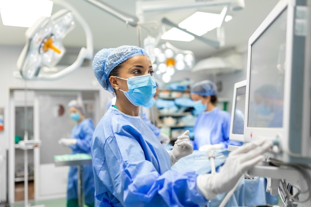 Foto anestesista que trabaja en el quirófano usando monitores de control de equipo protector mientras seda al paciente antes del procedimiento quirúrgico en el hospital