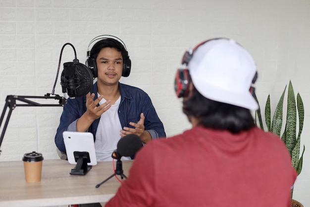 Foto anfitrião entrevistando músico no ar na sala de podcast usando microfone e smartphone em transmissão doméstica