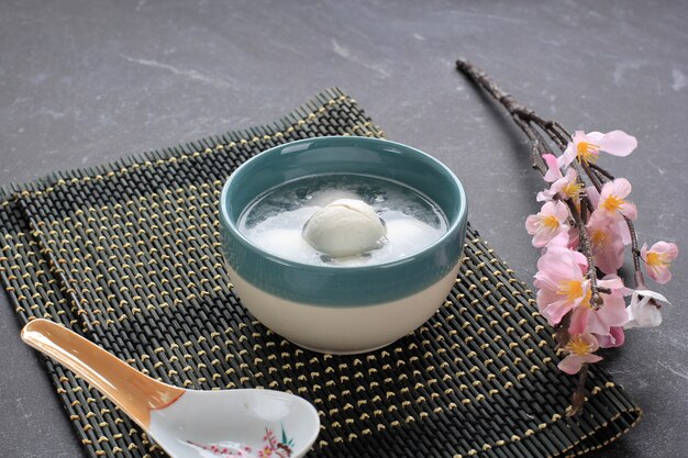 Ang Yuan (Wedang Ronde), chinesische Klebreis-Knödelbällchen mit Zucker-Ingwer oder Palmzuckersirup auf rotem Chinesen auf schwarzem Hintergrund für Wintersonnenwende-Neujahrsfest-Essen.