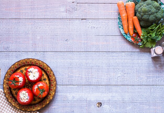 Angefüllte Tomaten mit Käse und unterschiedliches Gemüse auf einem Holztisch