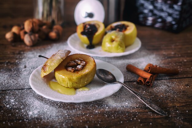 Angefüllter Bratapfel mit Nüssen, Honig und Schokolade auf weißen Nachtischtellern, dunkler hölzerner Hintergrund. Weihnachten süß. gesundes Essenkonzept.