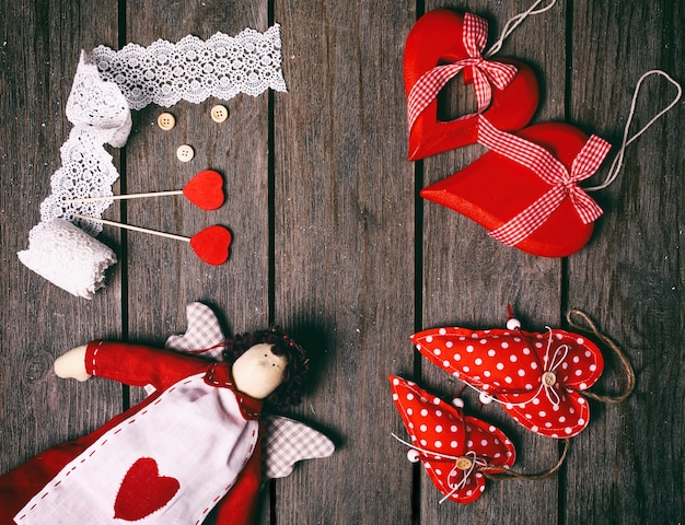 Foto angel un peluche con corazón, cinta de encaje, botones y tres corazones rojos sobre fondo de madera vieja. concepto de san valentín. vista superior.