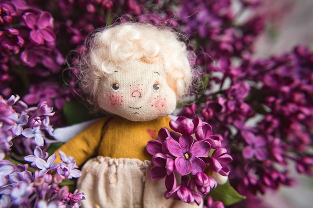 Foto angelito de cabello dorado en las flores de color azul, rosa, violeta, lila violeta. juguete hecho a mano en colores violetas lilas. tarjeta de felicitación.