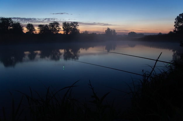 Angeln am nebligen See am frühen Morgen kurz vor Sonnenaufgang.