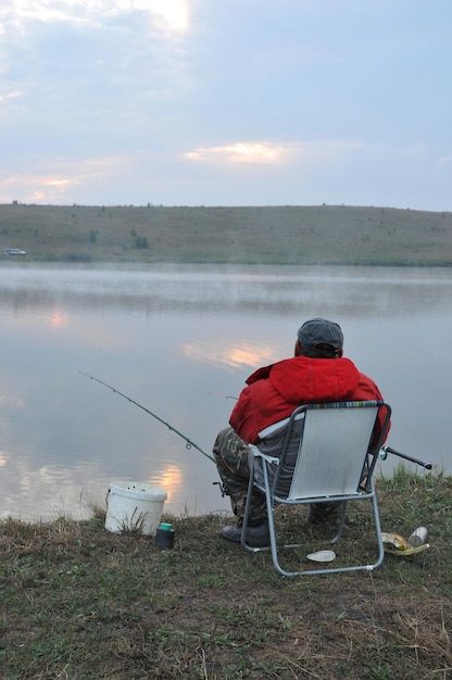 Foto angeln bei sonnenaufgang auf dem see fischer sitzt auf einem stuhl und angelt