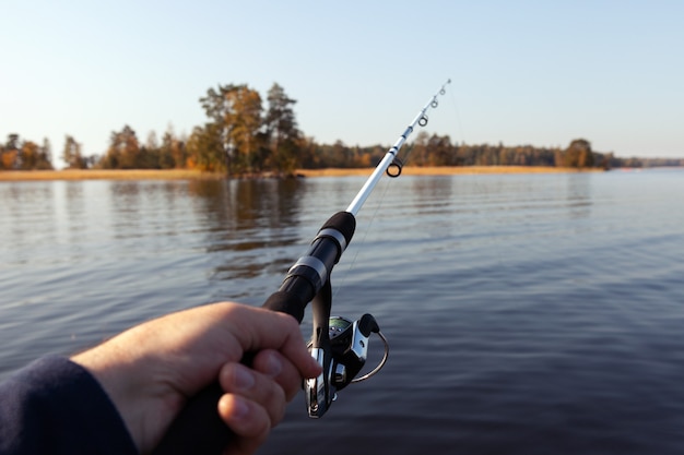 Foto angelrute in der hand auf dem hintergrund der herbstinsel. angeln am see.