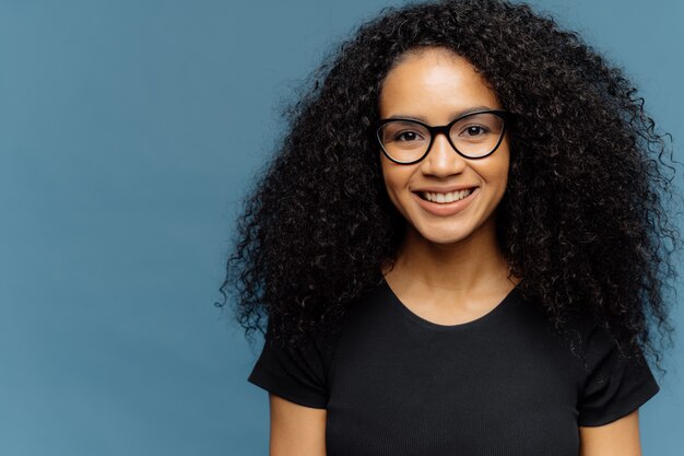 Angenehm aussehende dunkelhäutige Frau mit Afro-Frisur, transparenter Brille und lässigem schwarzem T-Shirt