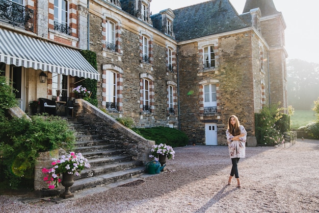 Angenehm aussehende Frau trägt Mantel und Hose steht vor großen Backstein alten Gebäude oder Schloss