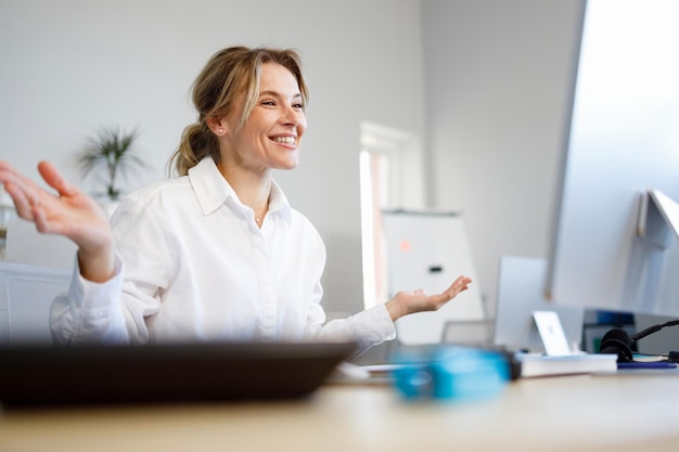 Angenehme Geschäftsfrau, die über einen Videoanruf spricht, während sie am Arbeitsplatz im Büro sitzt