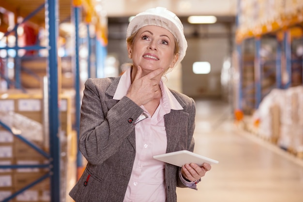 Angenehme nette Frau, die über die Problemlösung nachdenkt, während sie als Lagerhausmanager arbeitet