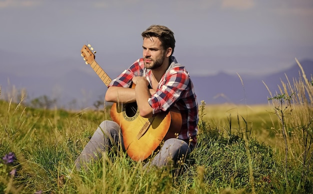 Angenehme Zeit allein Friedliche Stimmung Typ mit Gitarre betrachtet die Natur Fernweh-Konzept Inspirierende Natur Sommerurlaub Hochlandnatur Musiker auf der Suche nach Inspiration Verträumter Wanderer